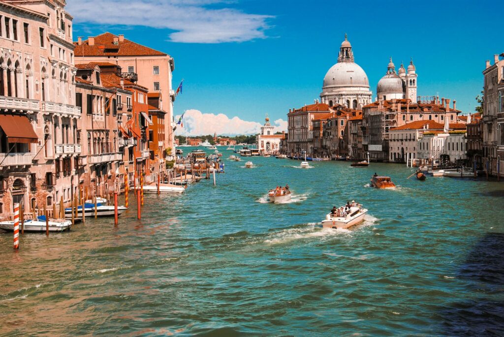 Vue du Grand Canal à Venise avec des bateaux naviguant entre des bâtiments historiques et la basilique Santa Maria della Salute sous un ciel bleu clair.
