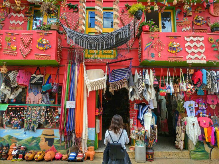 Une boutique artisanale colorée dans une rue colombienne, remplie de textiles traditionnels, de sacs, de hamacs et de décorations accrochées à une façade rouge ornée.