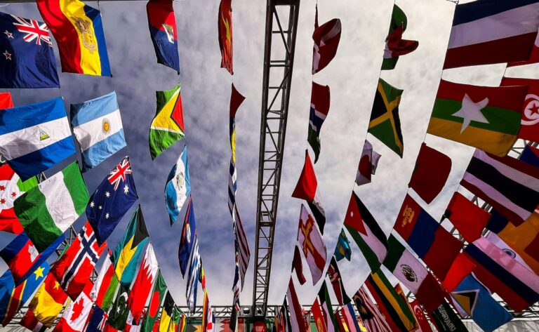 Drapeaux de différents pays suspendus en rangées sous un ciel légèrement nuageux, symbolisant la diversité et l’unité internationale