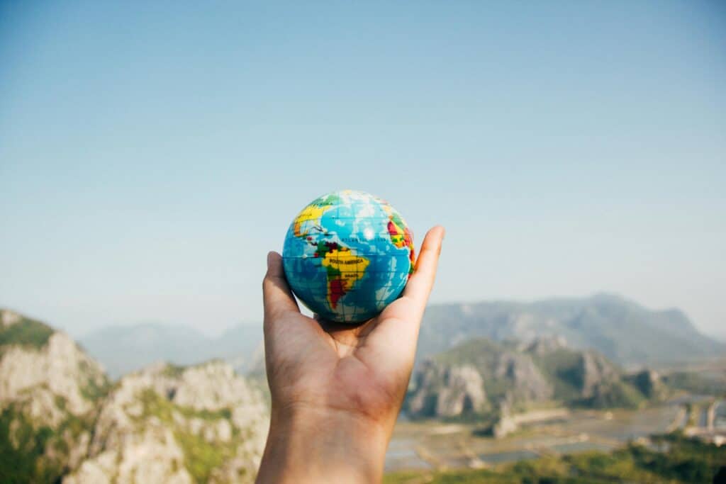 Une main tenant un globe terrestre miniature devant un paysage naturel avec des montagnes en arrière-plan, symbolisant l'exploration et le voyage.
