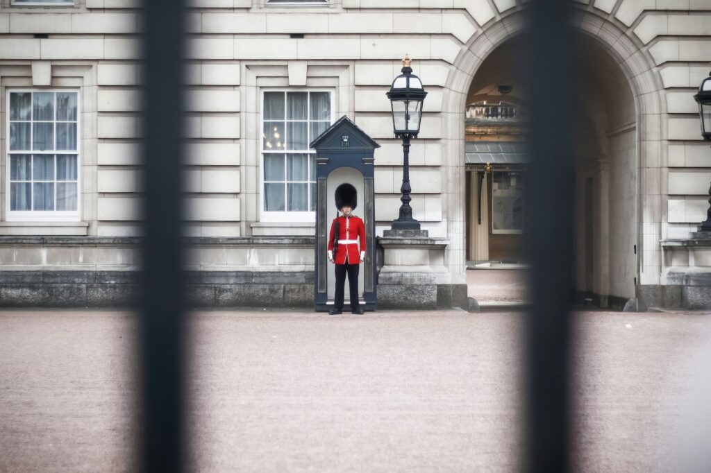 : "Garde royal en uniforme rouge traditionnel devant un poste de garde à Buckingham Palace, Londres, Royaume-Uni.