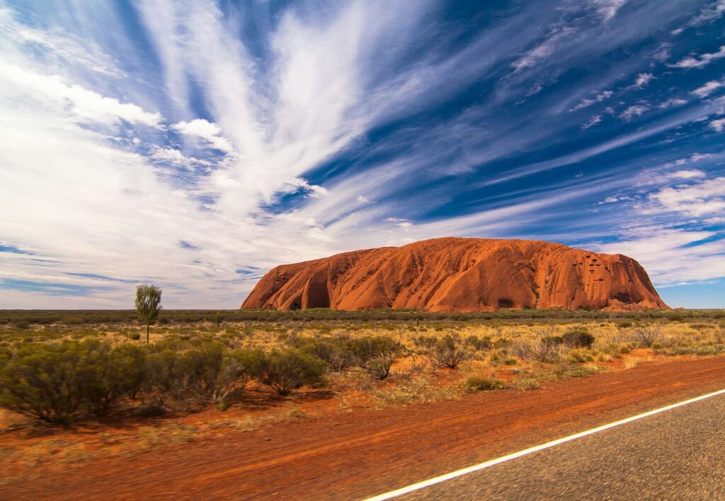 Paysage emblématique d'Uluru, un rocher rouge au cœur de l'Australie sous un ciel bleu parsemé de nuages