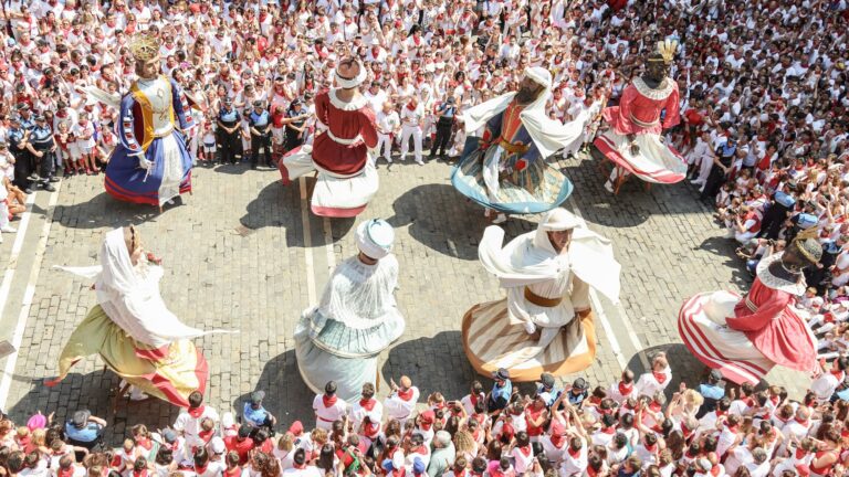 éants costumés défilant et dansant lors des fêtes de San Fermín à Pampelune, entourés par une foule vêtue de blanc et rouge